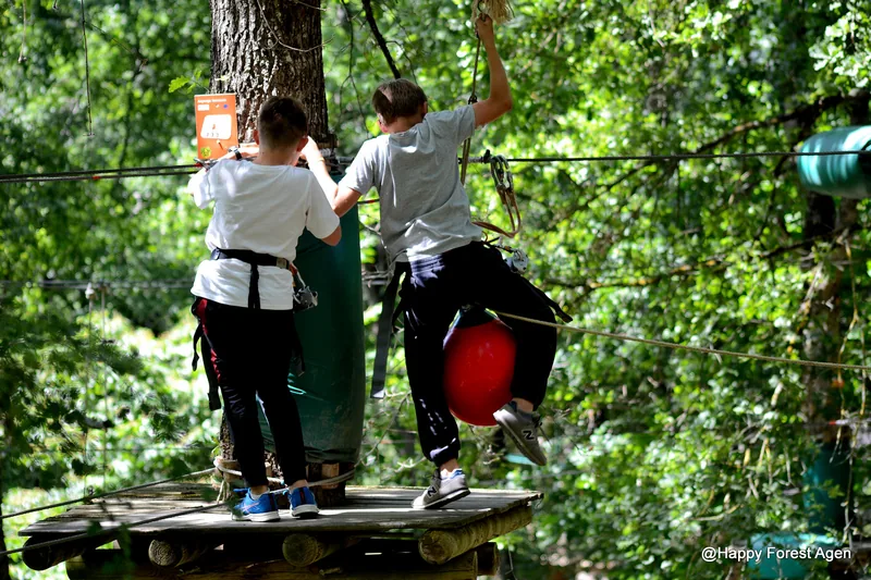 Deux enfants harnachés progressent sur une plateforme d'accrobranche dans les chênes de Happy Forest